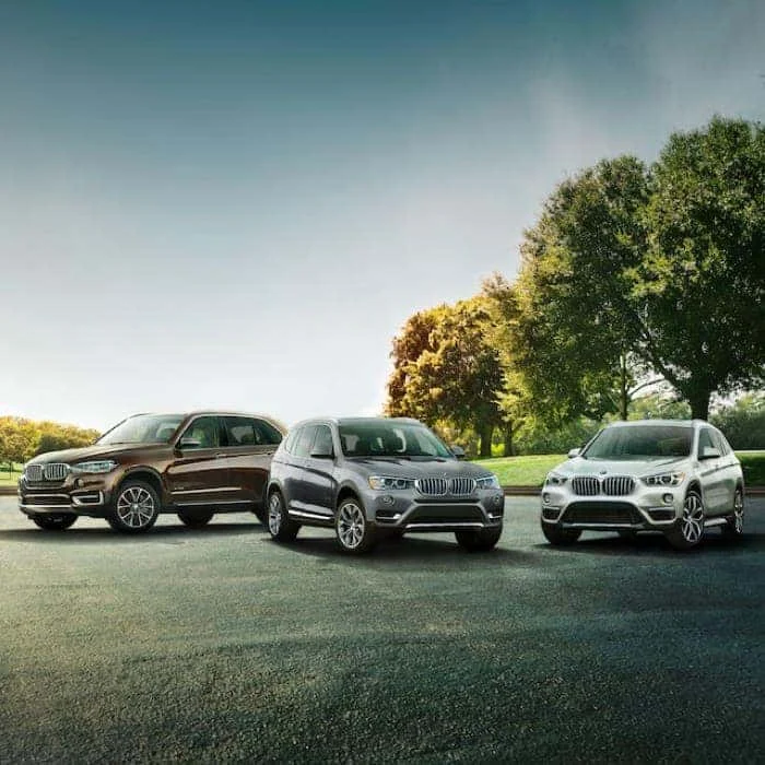 Three BMW vehicles are parked on a lot next to trees